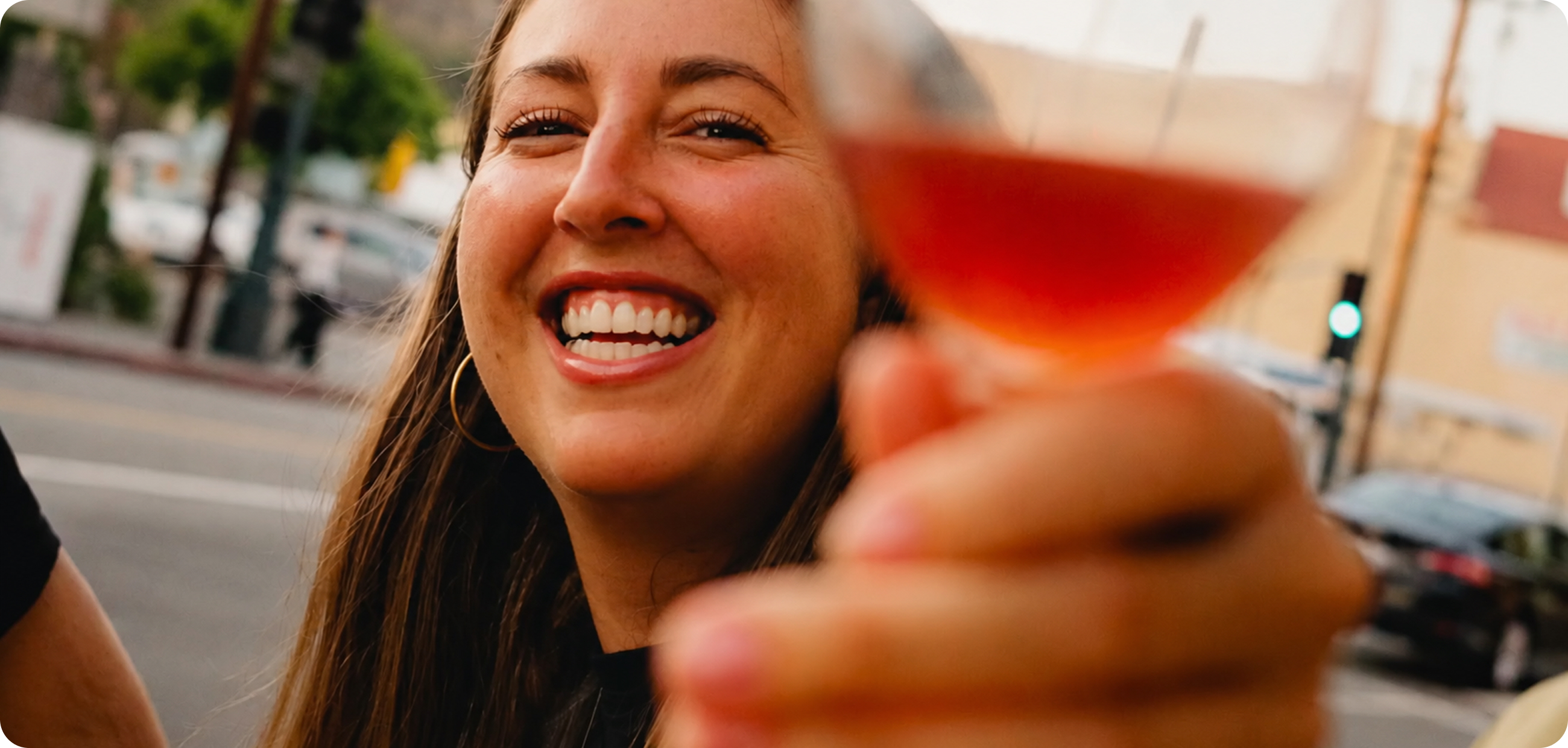 Junge Frau stößt auf der Straße mit einem Glas an.